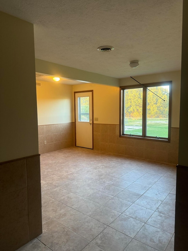 tiled empty room featuring a textured ceiling and tile walls