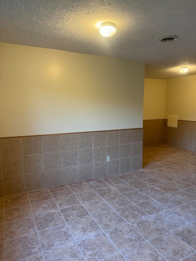 empty room with light tile patterned flooring, tile walls, and a textured ceiling