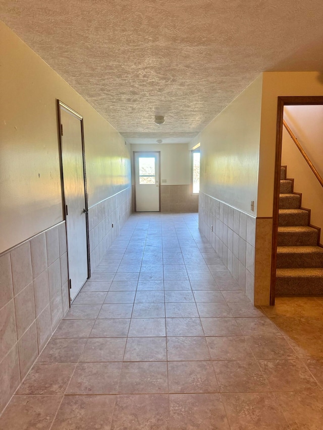 corridor featuring a textured ceiling, tile walls, and light tile patterned floors