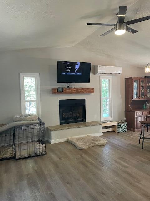 living room with a healthy amount of sunlight, a wall unit AC, vaulted ceiling, and wood-type flooring