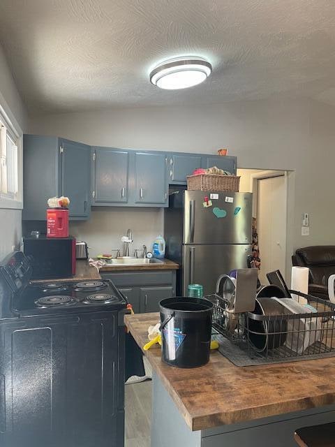 kitchen featuring stainless steel fridge, black range with electric cooktop, sink, and a textured ceiling