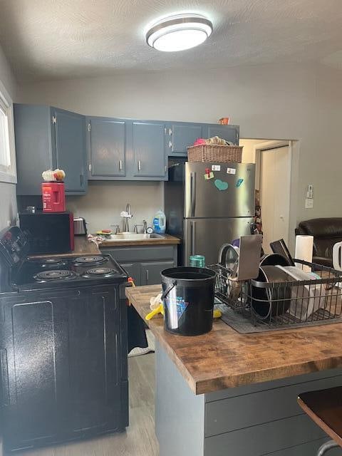 kitchen with black range with electric stovetop, sink, a textured ceiling, stainless steel refrigerator, and butcher block counters