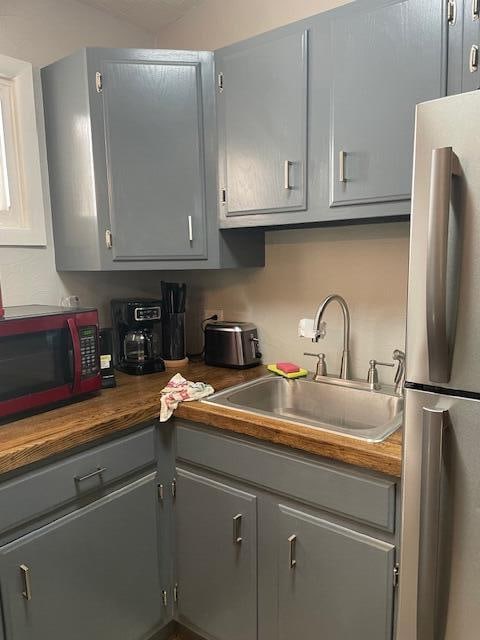 kitchen featuring butcher block counters, gray cabinets, stainless steel refrigerator, and sink