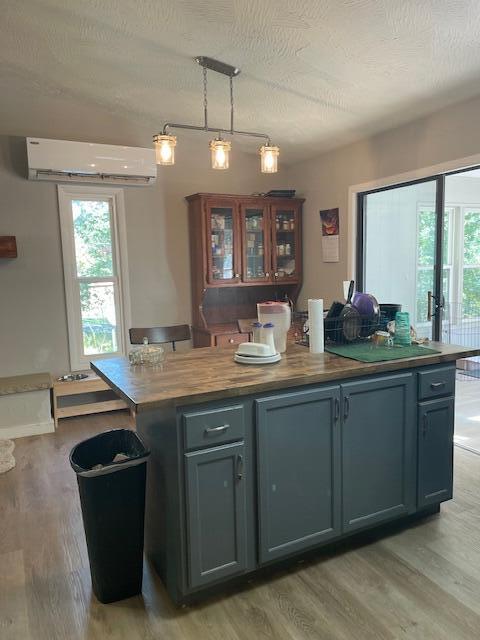 kitchen with wooden counters, a kitchen island, decorative light fixtures, a wall mounted air conditioner, and a textured ceiling