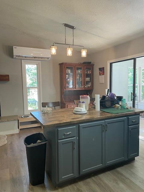 kitchen with decorative light fixtures, butcher block counters, a wall mounted AC, a center island, and a textured ceiling