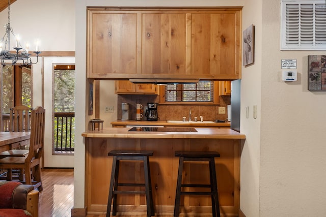 bar featuring black electric cooktop, decorative backsplash, hardwood / wood-style flooring, sink, and decorative light fixtures