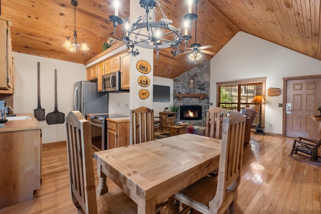 dining space featuring a stone fireplace, light wood-type flooring, high vaulted ceiling, and wooden ceiling