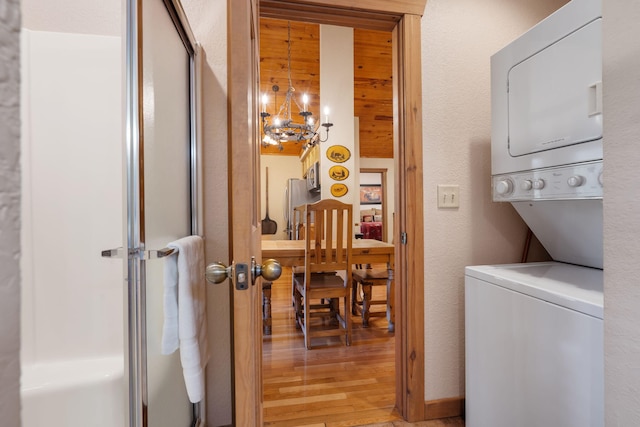 washroom with light wood-type flooring, stacked washer / dryer, and a chandelier