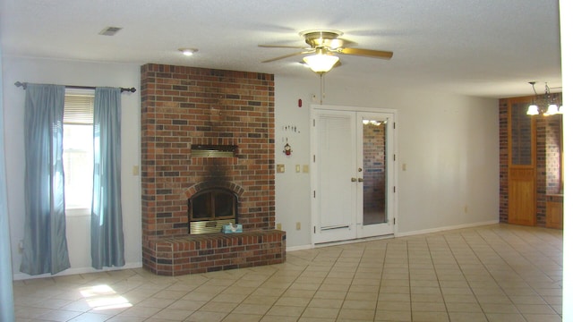 unfurnished living room featuring ceiling fan with notable chandelier, a brick fireplace, light tile patterned floors, and a textured ceiling