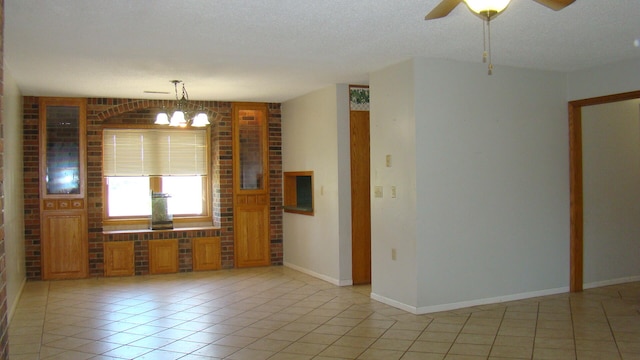 empty room featuring brick wall, a textured ceiling, ceiling fan with notable chandelier, and light tile patterned floors