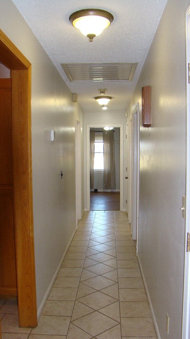 hall with a textured ceiling and light tile patterned floors