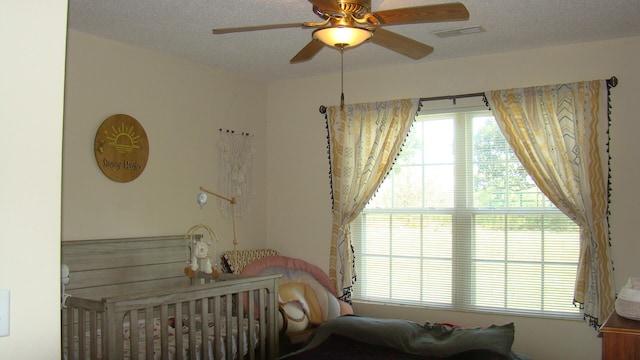 bedroom featuring ceiling fan, a crib, and a textured ceiling