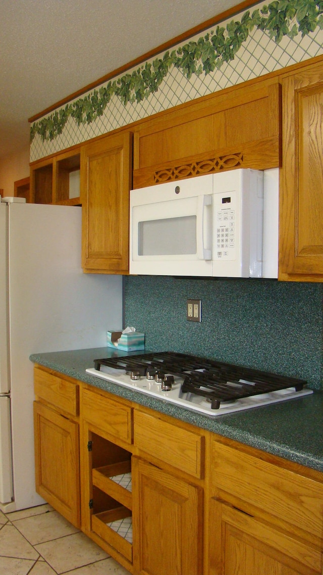 kitchen featuring backsplash, light tile patterned floors, and white appliances