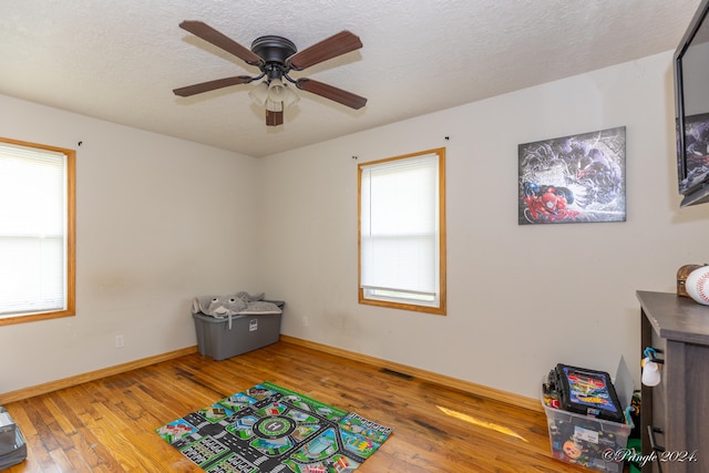 recreation room featuring hardwood / wood-style flooring, a textured ceiling, and ceiling fan