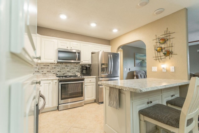 kitchen with tasteful backsplash, a breakfast bar, light stone counters, white cabinets, and appliances with stainless steel finishes