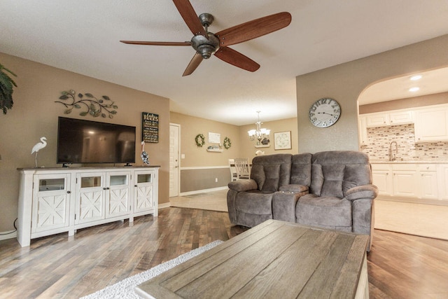 living room with wood-type flooring, ceiling fan with notable chandelier, and sink