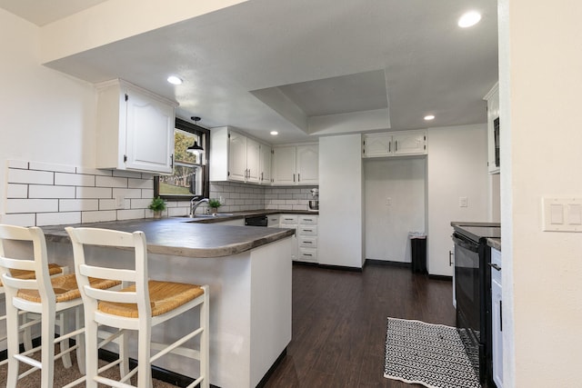 kitchen with dark wood-type flooring, sink, kitchen peninsula, white cabinets, and black appliances