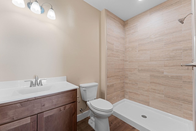 bathroom with hardwood / wood-style floors, a tile shower, vanity, and toilet