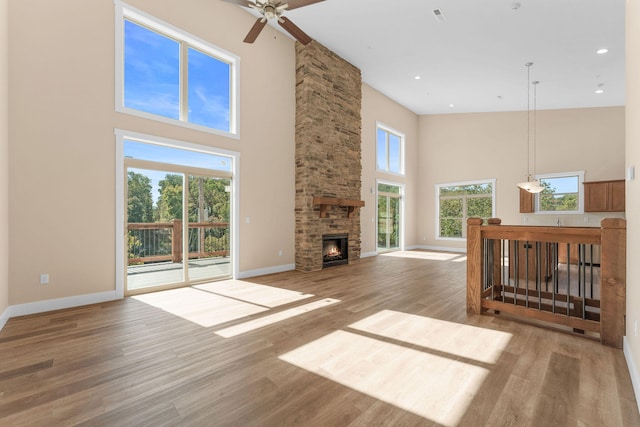 unfurnished living room with a towering ceiling, ceiling fan, light hardwood / wood-style flooring, and a stone fireplace