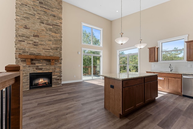 kitchen with pendant lighting, a kitchen island, dark wood-type flooring, light stone counters, and dishwasher