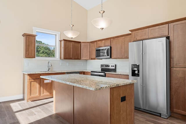 kitchen with hardwood / wood-style floors, stainless steel appliances, light stone countertops, hanging light fixtures, and high vaulted ceiling