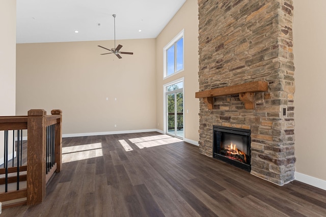 unfurnished living room featuring ceiling fan, a fireplace, dark hardwood / wood-style floors, and a high ceiling