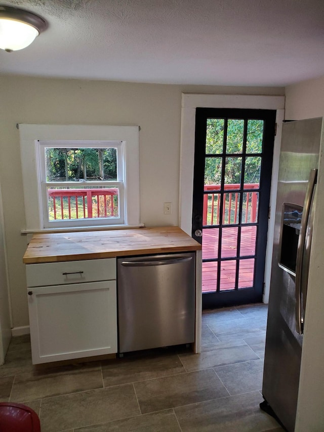 kitchen featuring wooden counters, a healthy amount of sunlight, white cabinets, and dishwasher