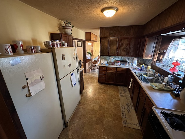 kitchen with stove, decorative backsplash, sink, white fridge, and a textured ceiling