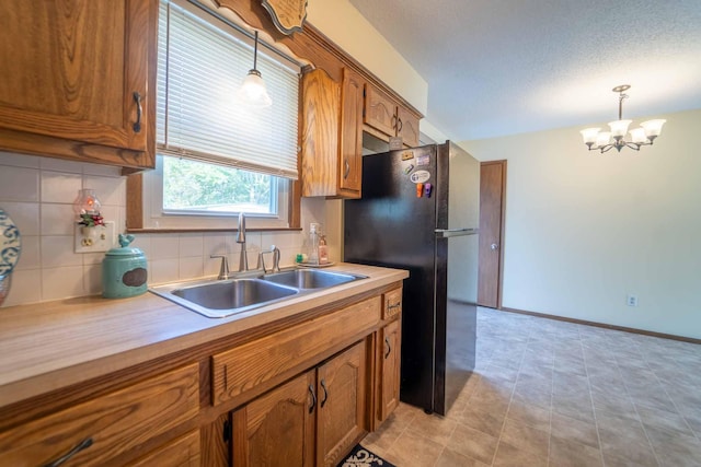 kitchen featuring tasteful backsplash, sink, black refrigerator, pendant lighting, and a notable chandelier