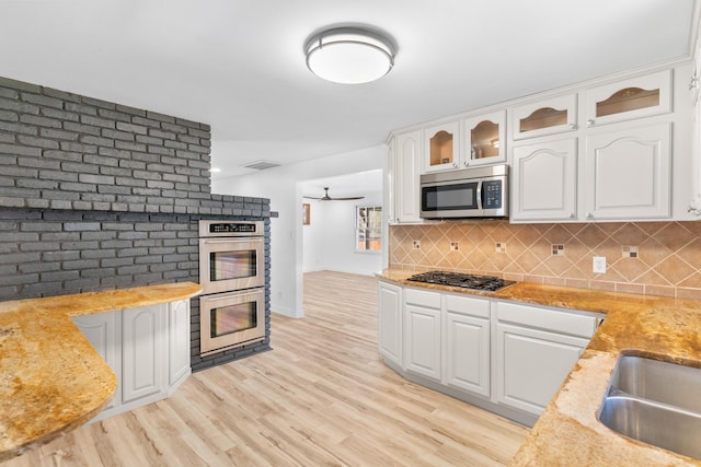 kitchen featuring light stone countertops, tasteful backsplash, white cabinetry, light wood-type flooring, and stainless steel appliances