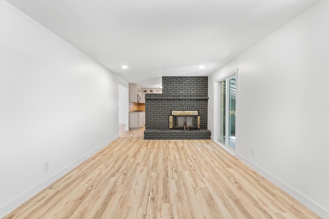 unfurnished living room with a brick fireplace and light hardwood / wood-style flooring