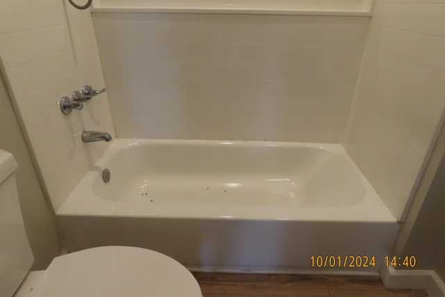 bathroom with washtub / shower combination, wood-type flooring, and toilet