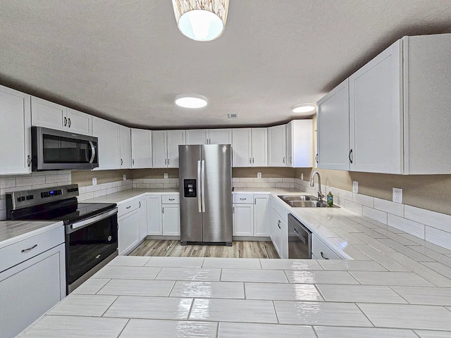 kitchen with sink, light hardwood / wood-style floors, white cabinetry, appliances with stainless steel finishes, and a textured ceiling