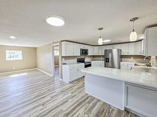 kitchen featuring stainless steel appliances, white cabinets, kitchen peninsula, hanging light fixtures, and light hardwood / wood-style flooring