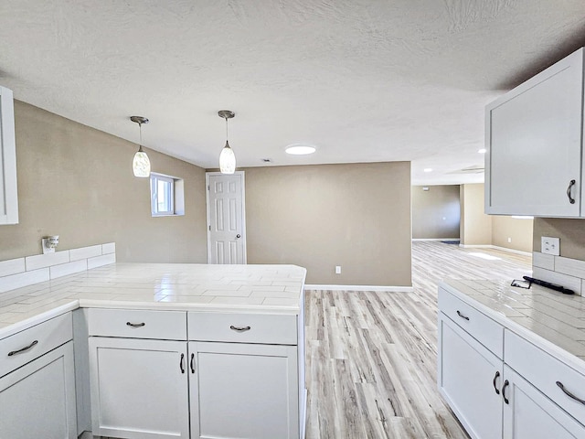 kitchen featuring light wood-type flooring, kitchen peninsula, white cabinetry, decorative light fixtures, and a textured ceiling