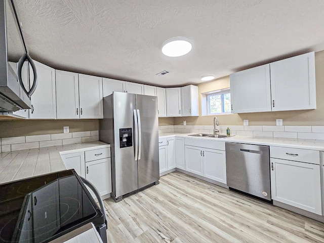 kitchen with light wood-type flooring, stainless steel appliances, sink, white cabinetry, and a textured ceiling