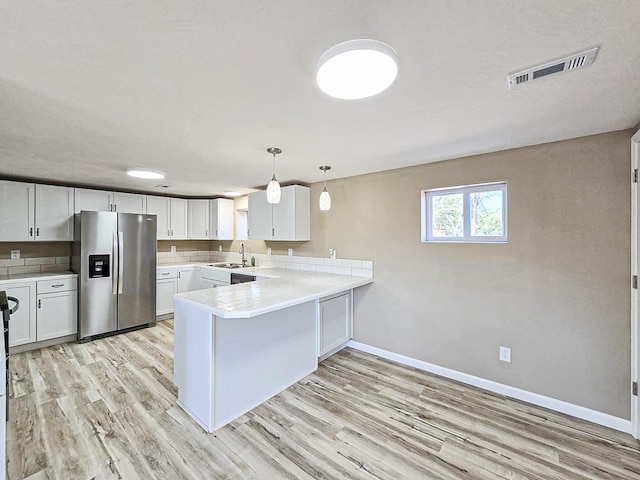 kitchen featuring sink, kitchen peninsula, hanging light fixtures, stainless steel refrigerator with ice dispenser, and white cabinetry