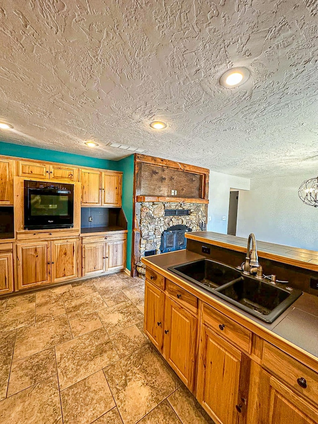 kitchen featuring a stone fireplace, a textured ceiling, sink, and oven