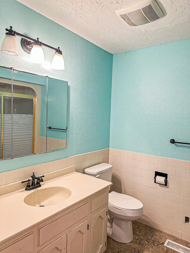 bathroom with vanity, a textured ceiling, tile walls, toilet, and a shower with door