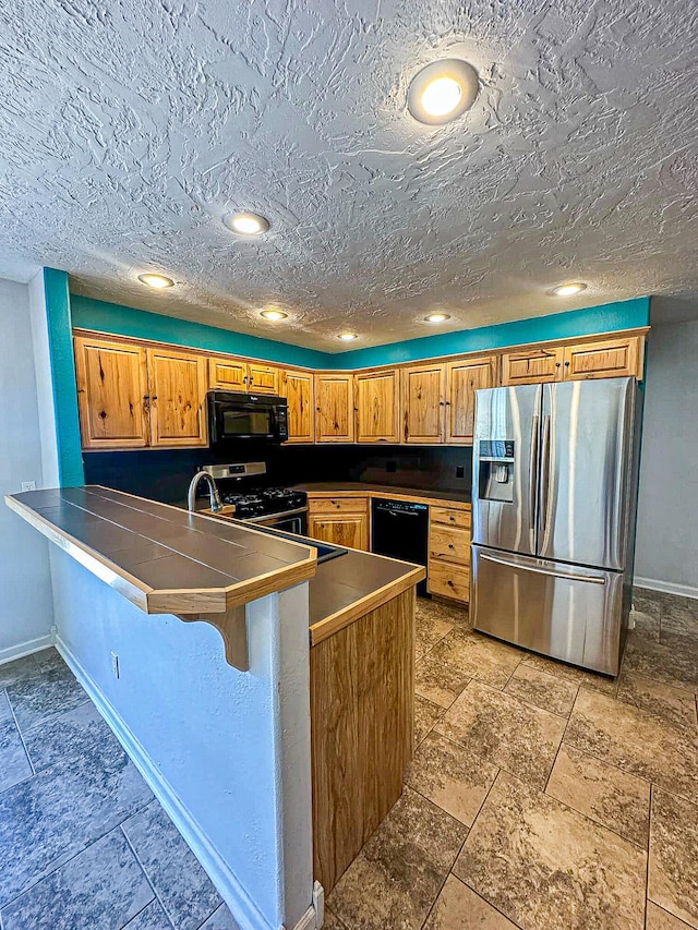 kitchen with a breakfast bar area, sink, kitchen peninsula, black appliances, and a textured ceiling