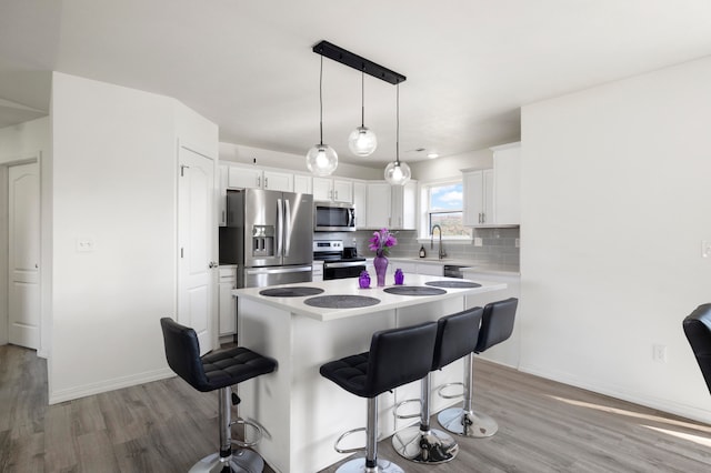 kitchen featuring white cabinets, a kitchen island, light hardwood / wood-style flooring, backsplash, and stainless steel appliances