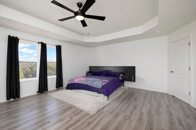 bedroom with a raised ceiling, light wood-type flooring, and ceiling fan