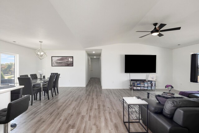 living room with ceiling fan with notable chandelier, vaulted ceiling, and light hardwood / wood-style flooring