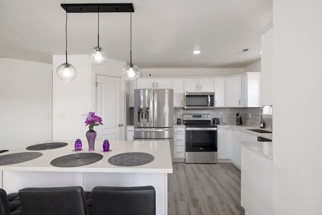 kitchen featuring pendant lighting, sink, white cabinetry, appliances with stainless steel finishes, and light wood-type flooring