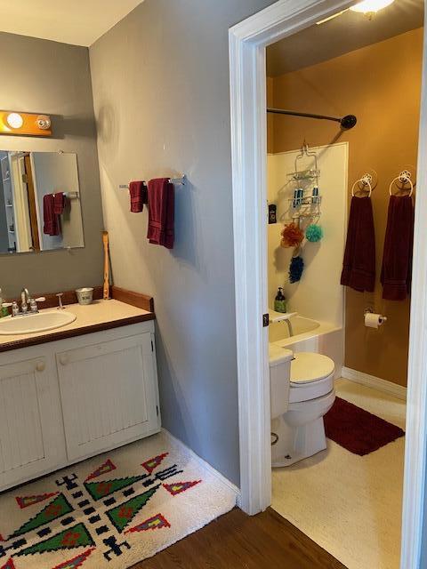 bathroom with wood finished floors, baseboards, toilet, shower / washtub combination, and vanity