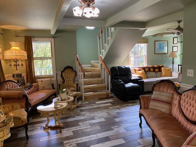 living area featuring beamed ceiling, a healthy amount of sunlight, stairs, and wood finished floors