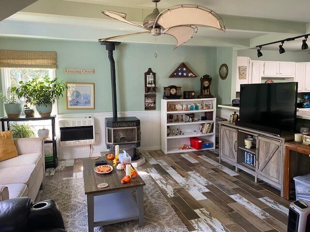 living room with track lighting, a wood stove, heating unit, dark hardwood / wood-style flooring, and ceiling fan