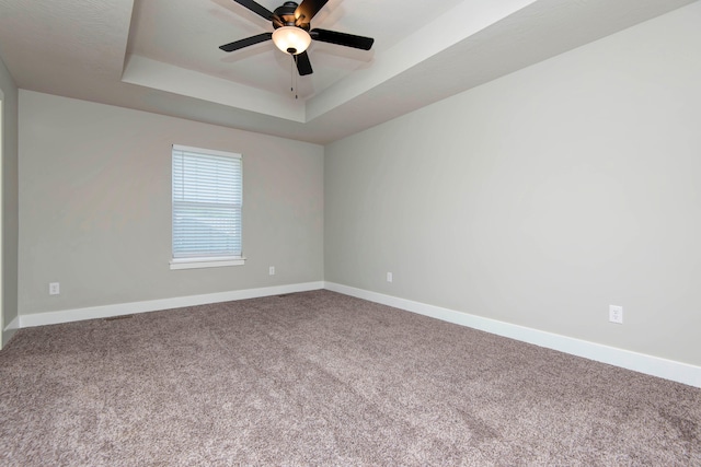 carpeted spare room with ceiling fan and a raised ceiling