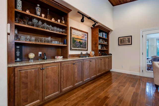 bar with light stone counters, sink, and dark wood-type flooring