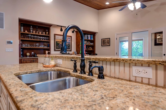 kitchen featuring light stone counters, ceiling fan, sink, wooden ceiling, and a towering ceiling